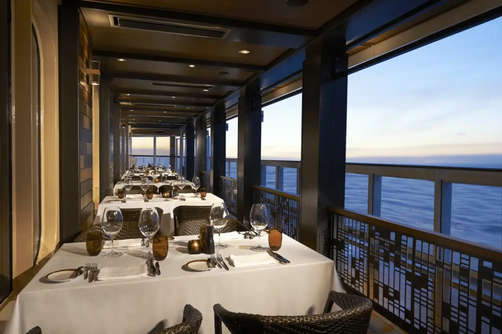 Interieur van een sfeervol restaurant aan boord van de Norwegian Bliss, met gedekte tafels en uitzicht op zee.