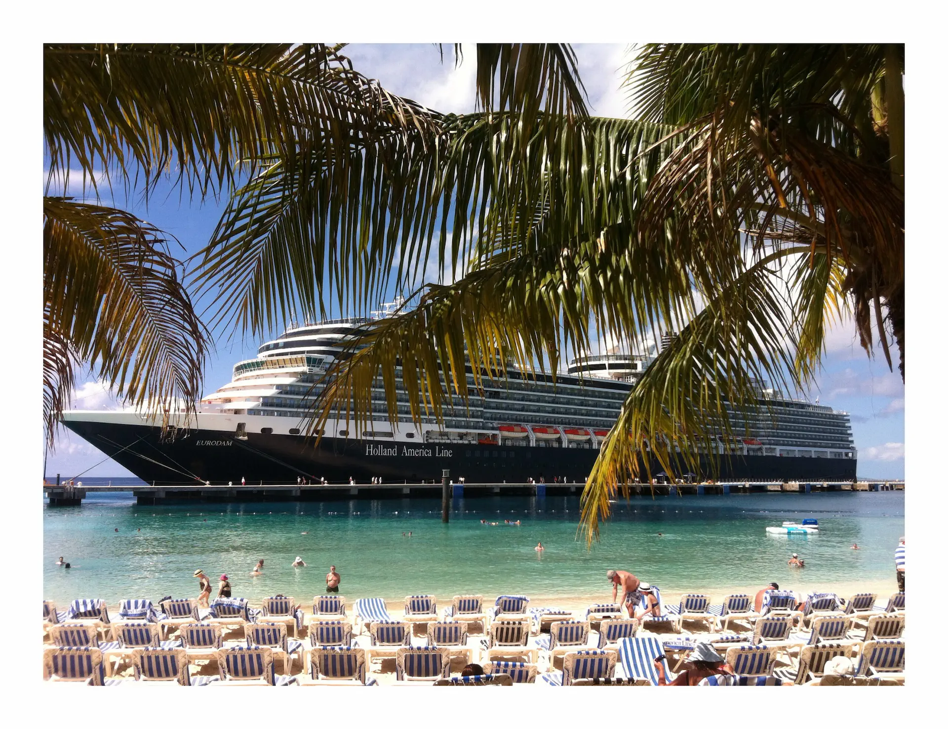 Cruiseschip voor anker bij een strand in Costa Rica, gezien tussen palmbomen met ligbedden op de voorgrond.