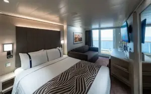 Luxe interieur van een World Atlantic Deluxe Balkonhut met een groot tweepersoonsbed, zithoek en uitzicht op de oceaan via het privébalkon.