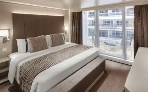 Interieur van de Deluxe Balkonhut Promenade op de World Atlantic met een groot bed en uitzicht op de binnenpromenade vanaf het privébalkon.