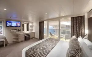 Slaapkamer van de Deluxe Suite SRP op de World Atlantic met uitzicht op de promenade en de zee vanaf het privébalkon.