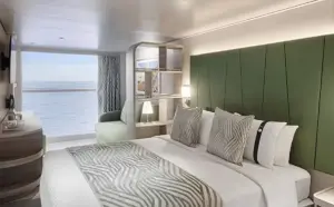 Modern interieur van de World Atlantic Infinite Buitenhut met een groen gecapitonneerd hoofdbord, zithoek en een kamerhoog raam met panoramisch zeezicht.