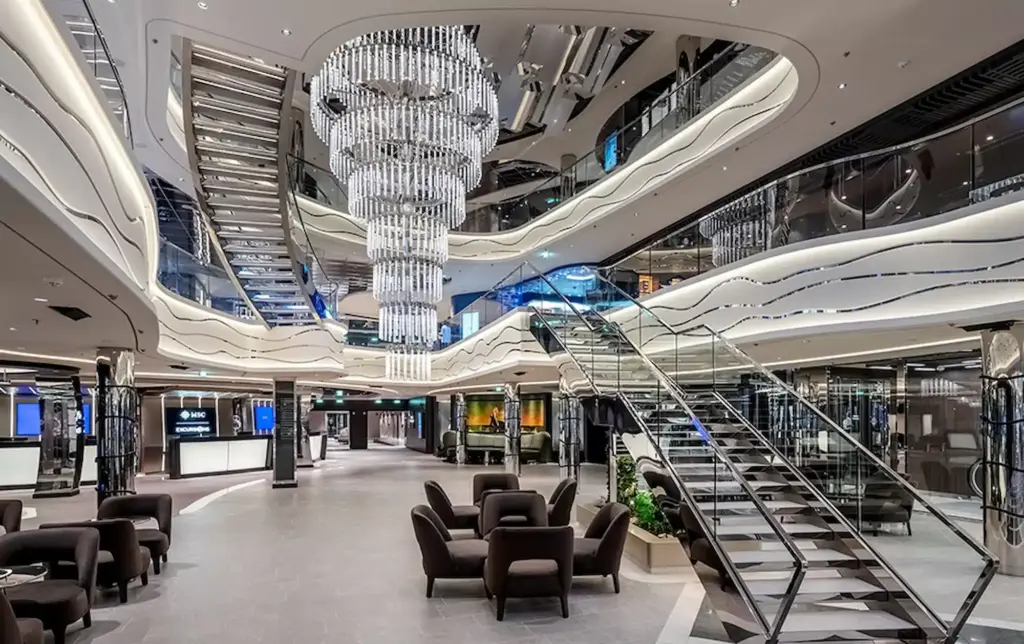 Het spectaculaire atrium van de MSC World Atlantic met een gigantische kristallen kroonluchter, moderne glazen trappen en een futuristisch wit-verlicht plafond.