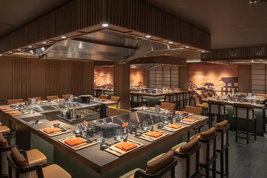 Interieur van het Teppanyaki restaurant op de MSC World Atlantic met grote kookplaten, moderne barstoelen en Japanse wandschilderingen.