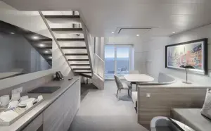 Moderne duplex woonkamer van de Yacht Club Suite op de MSC World Atlantic met een eettafel, trap naar de vide en uitzicht op zee.
