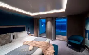 Interieur van de Yacht Club Owner's Suite slaapkamer op de MSC World Atlantic met een groot bed, blauwe wandpanelen en een privébalkon met zeezicht.